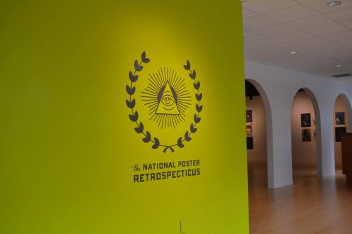 National Poster Retrospecticus exhibition wall with eye pyramid logo in yellow-green museum gallery with arched doorways