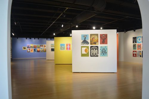 Contemporary art gallery exhibition with colorful paintings displayed on white walls and movable panels