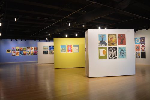 Art gallery exhibition with colorful wall displays featuring various artworks and prints on white and yellow panels