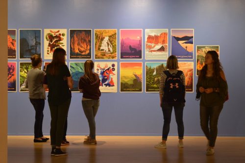 People viewing colorful national park poster collection displayed on museum wall featuring landscapes and wildlife art