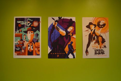 Three colorful movie posters on green wall featuring Toy Story, Hawkeye, and Cowboys & Aliens in retro artistic style