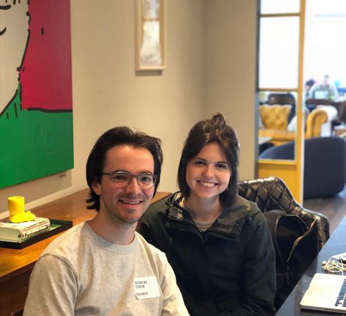 Two smiling people sitting together in a modern office with colorful wall art and yellow chairs in background