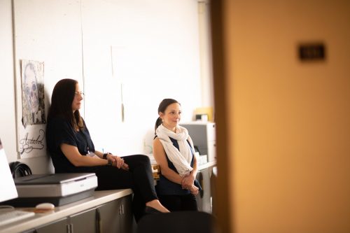 Two women having a friendly conversation while sitting on kitchen counter in bright modern home interior