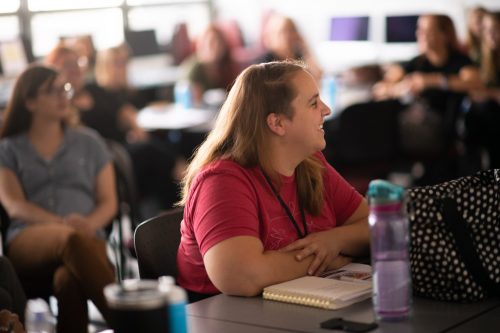 Woman in red shirt taking notes at professional development workshop or training session with other attendees