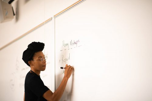 Woman with glasses writing Money Mishaps and Report on whiteboard during financial planning session