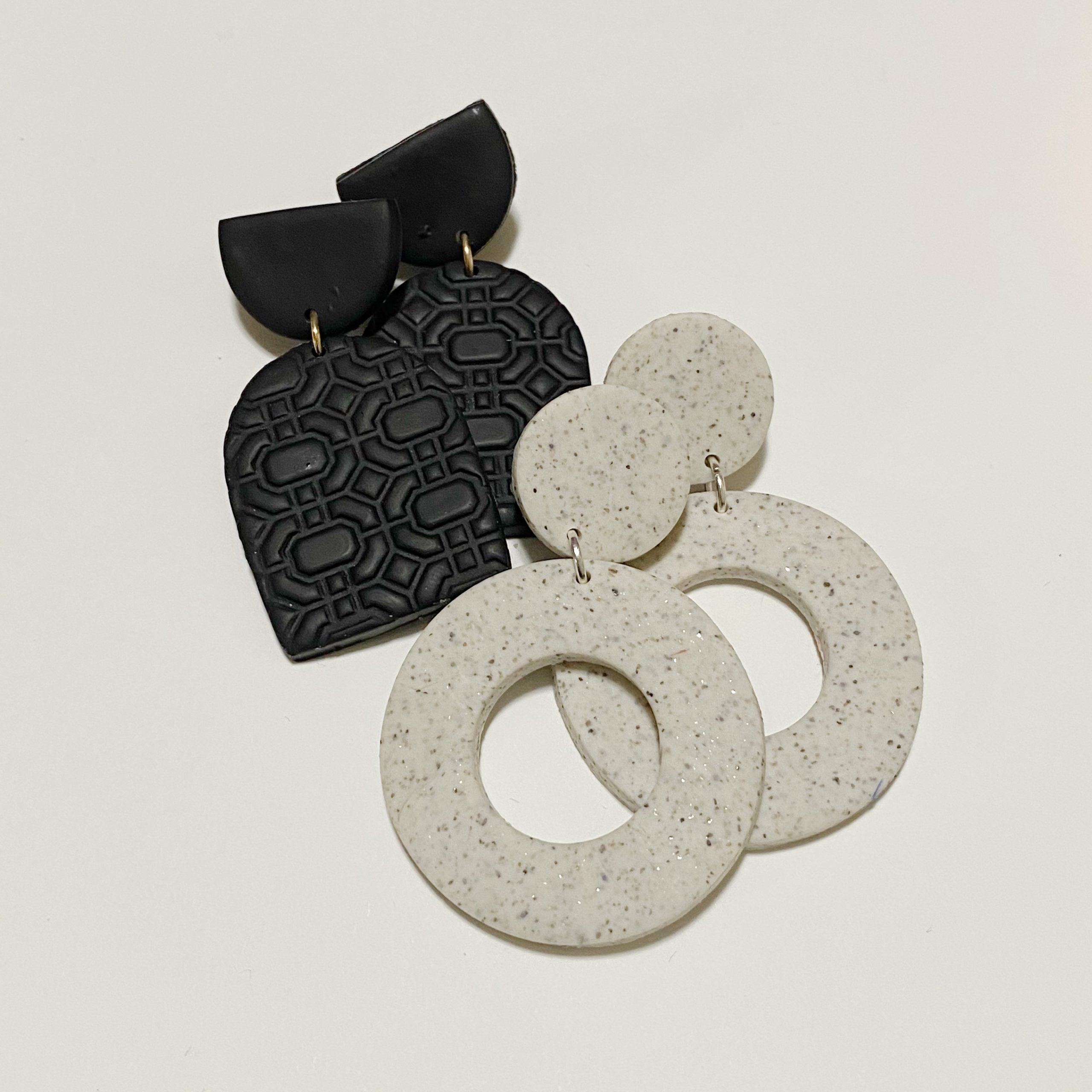Black textured polymer clay earrings and white speckled circle drop earrings with gold jump rings on white background