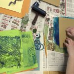 Person creating colorful printmaking art with green paper, ink roller, and various art supplies on newspaper-covered table
