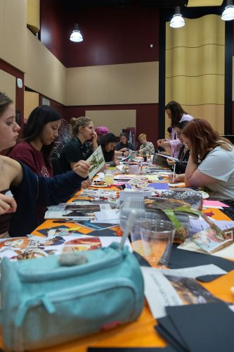 Women collaborating on creative project with photos and materials spread across orange table in modern workspace