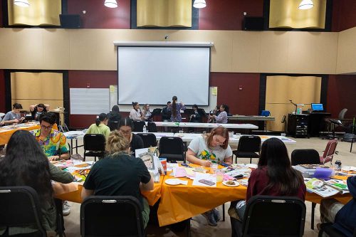 Workshop participants collaborate on creative projects at tables with colorful materials in modern conference room setting.