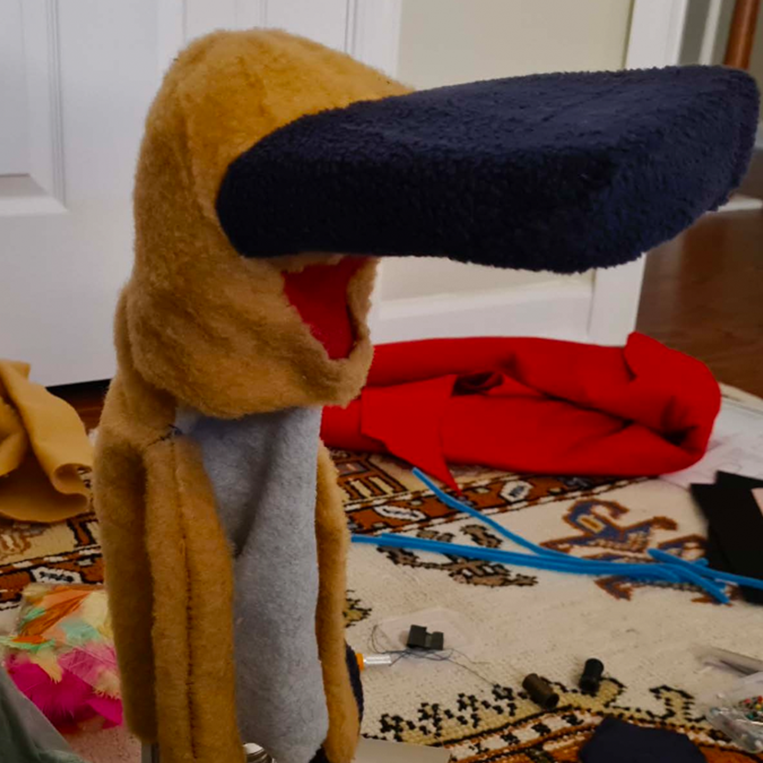 002-Prototype Colorful felt craft project with yellow duck head, navy blue beak, and red fabric on wooden chair with craft supplies