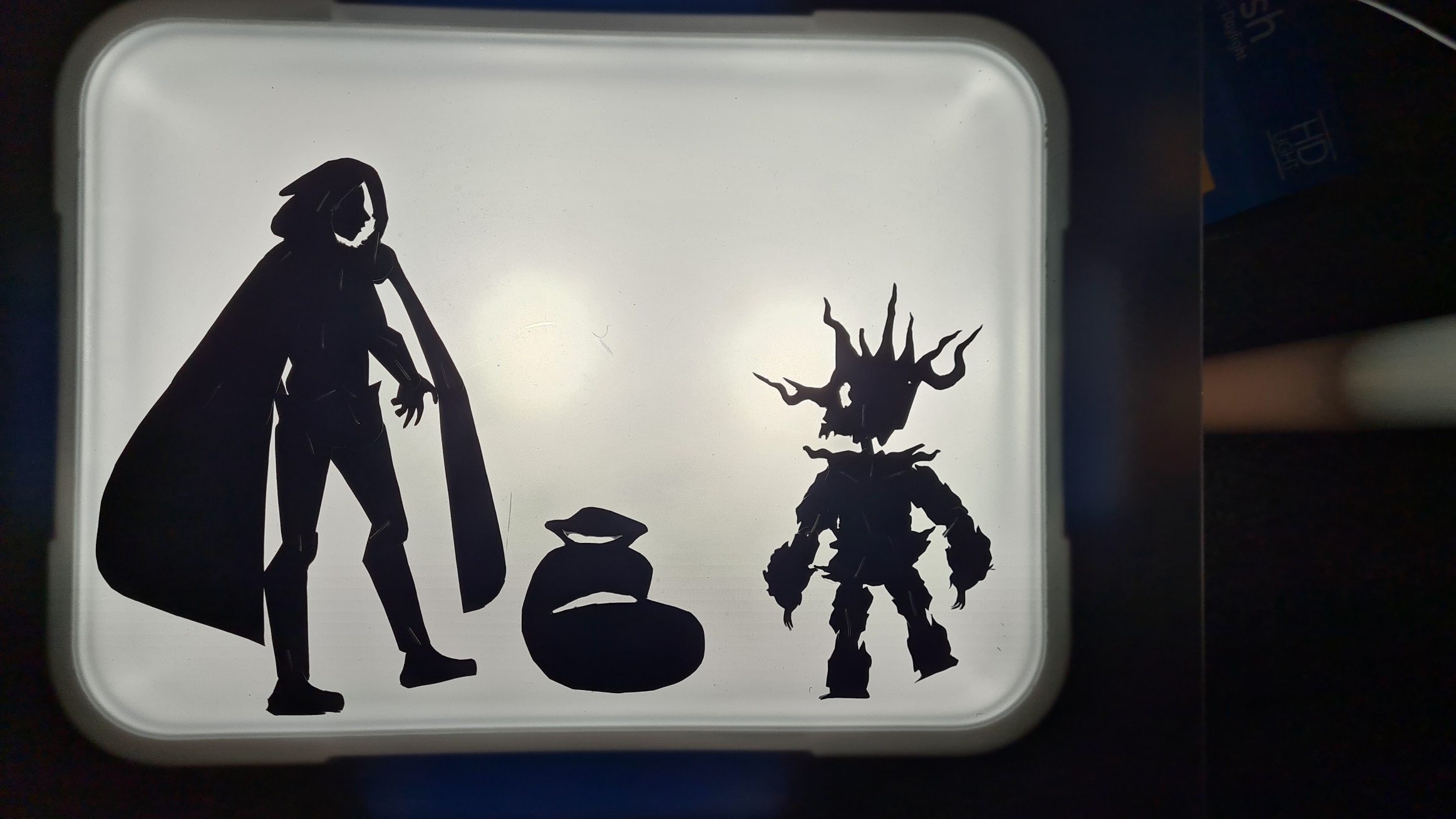 003-LightboxPuppetTest Black silhouette decals on white surface showing tall figure with cape next to spiky armored character and round objects