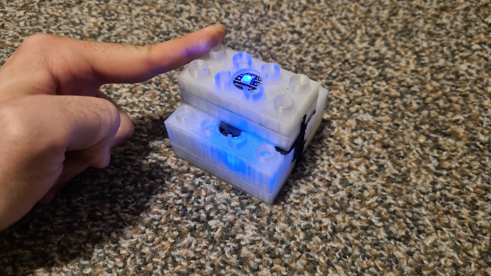 005-TestingFullCircuit Hand hovering over white 3D printed electronic device with blue LED lights on granite countertop surface