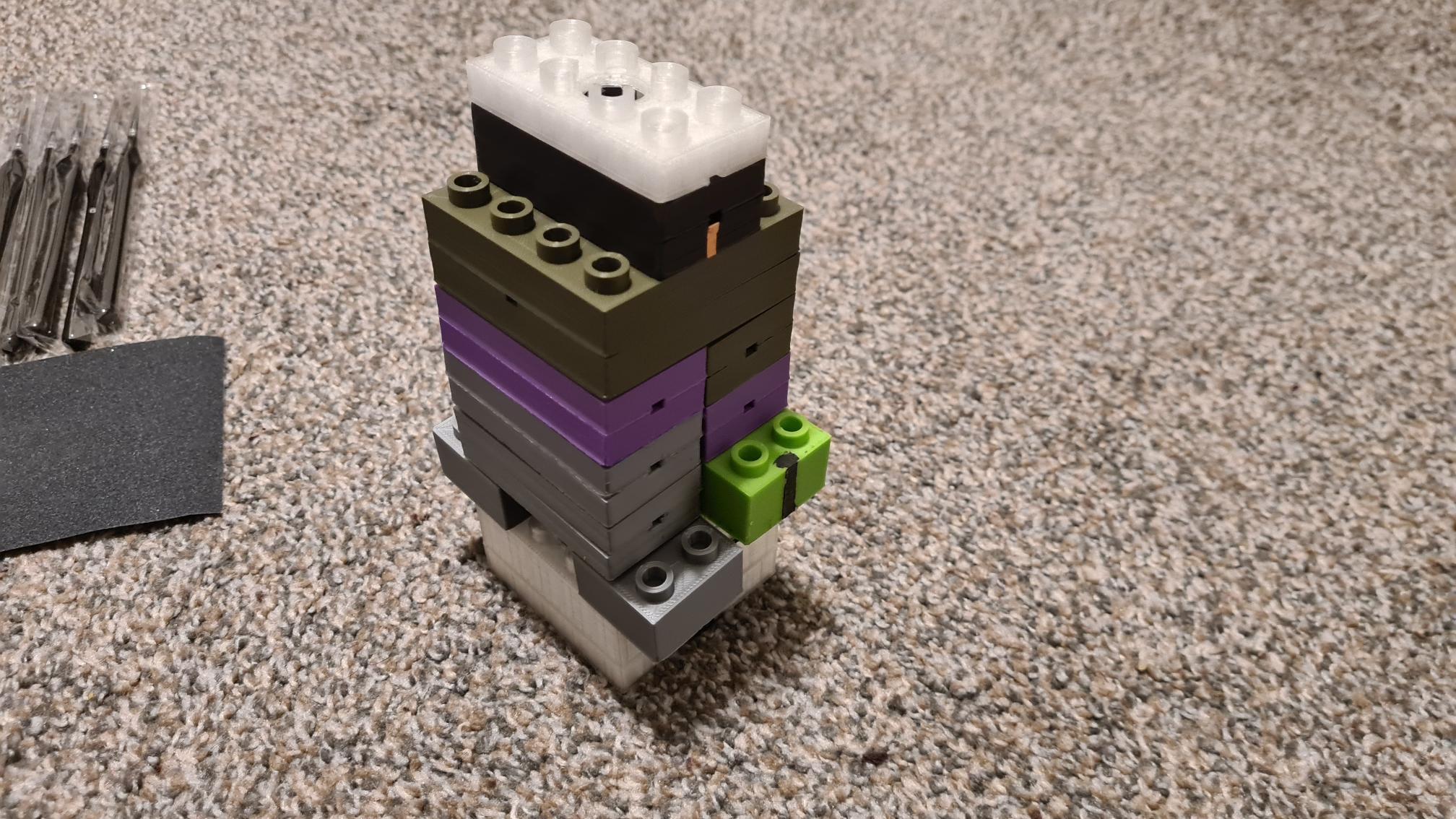 006-AllPrototypeBricks LEGO tower with white, black, green, purple and gray blocks stacked on carpeted floor