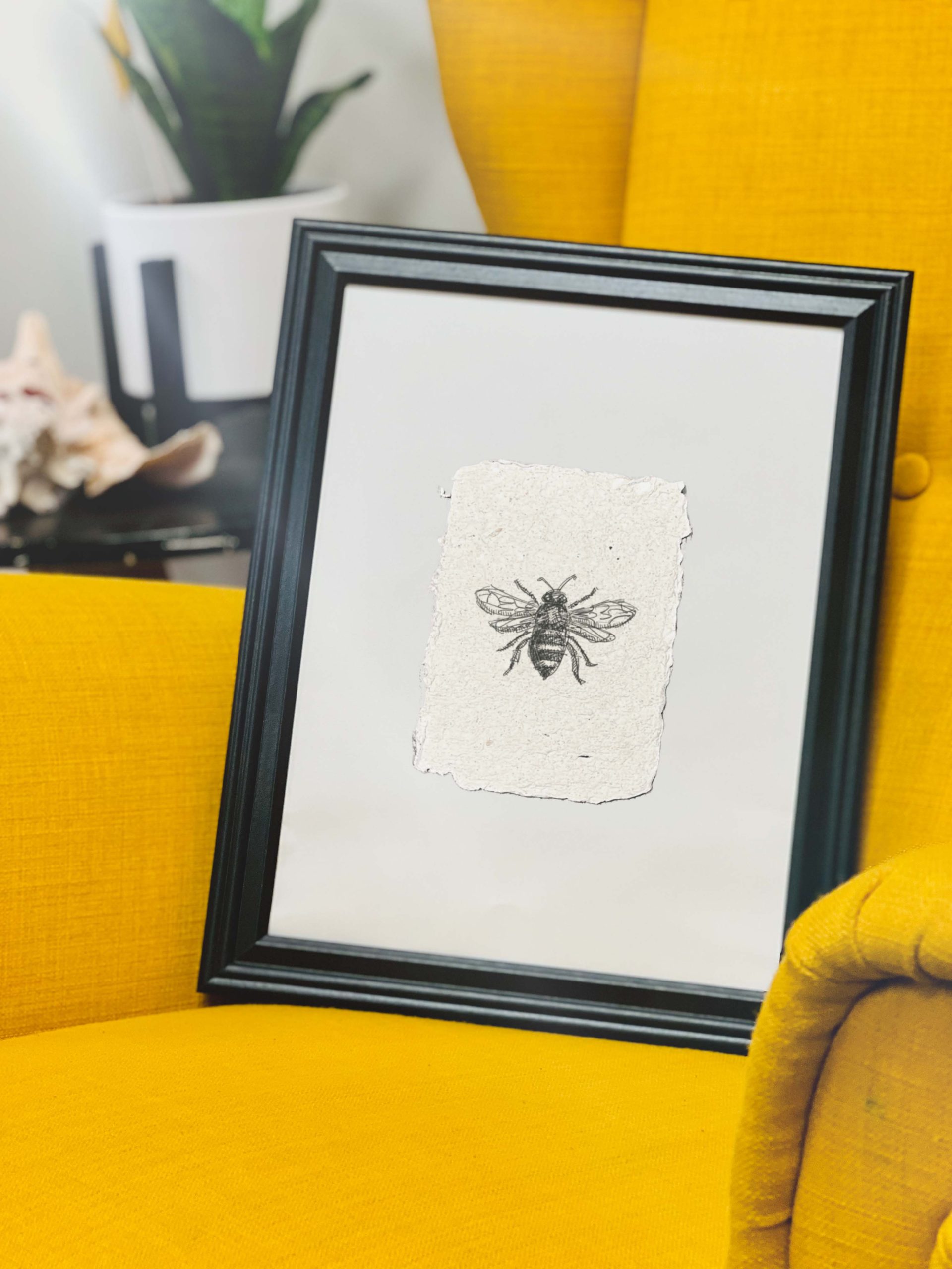 01 Framed bee artwork print in black frame on yellow couch with plant and cat in modern living room decor