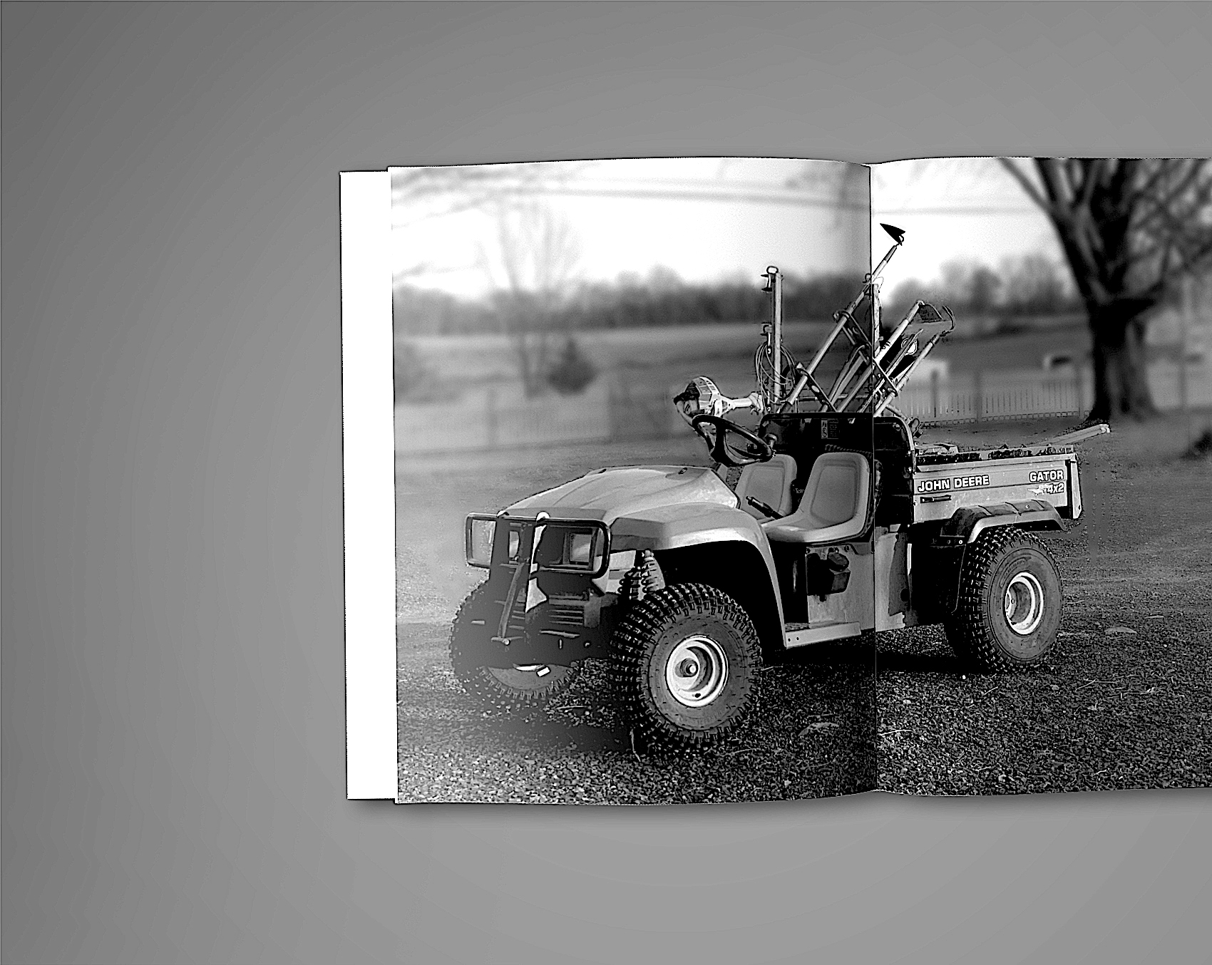 02 John Deere Gator utility vehicle with equipment attachments parked on farm road in black and white photograph