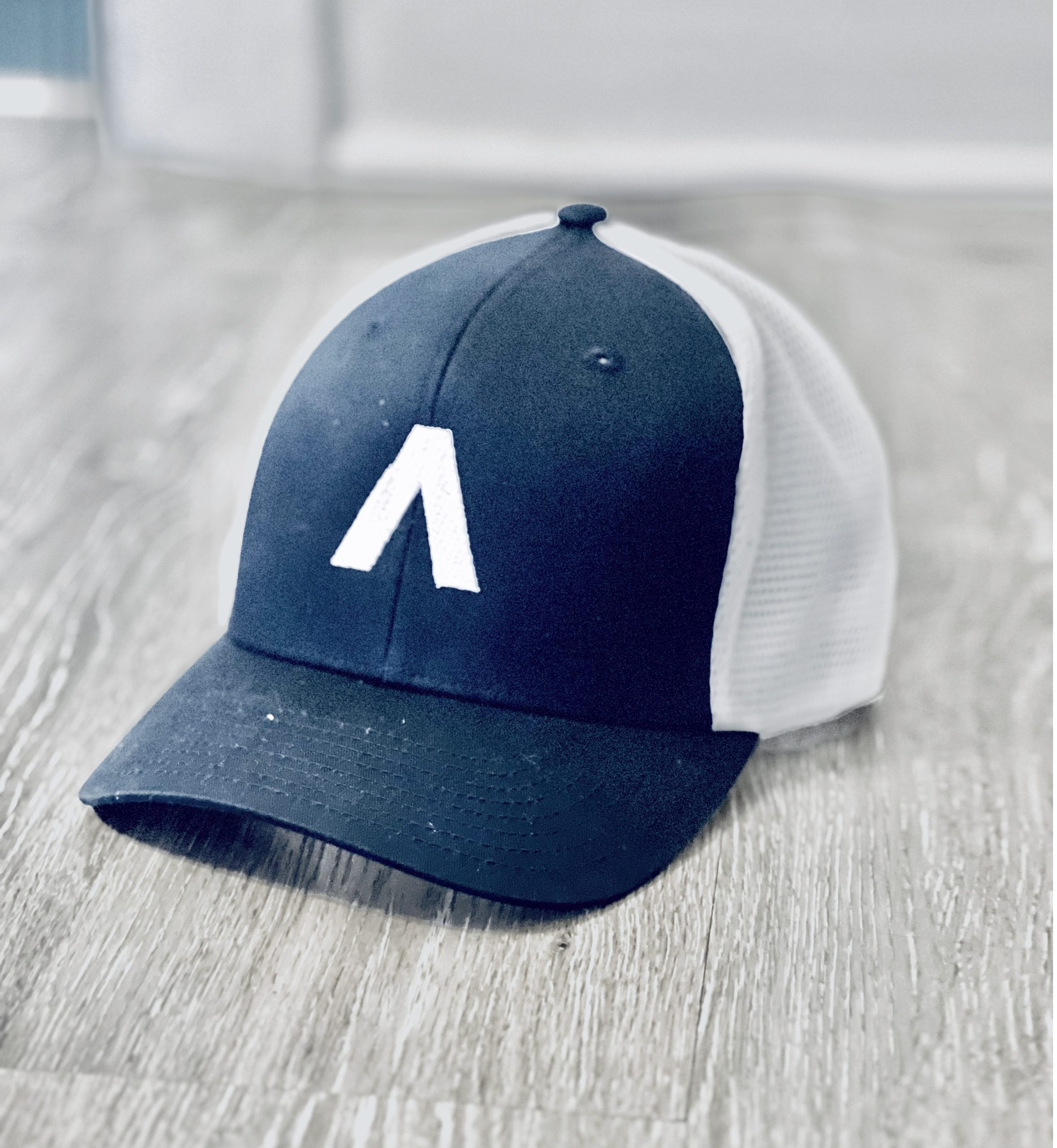 07 Navy blue and white trucker hat with letter A logo sitting on weathered wood surface