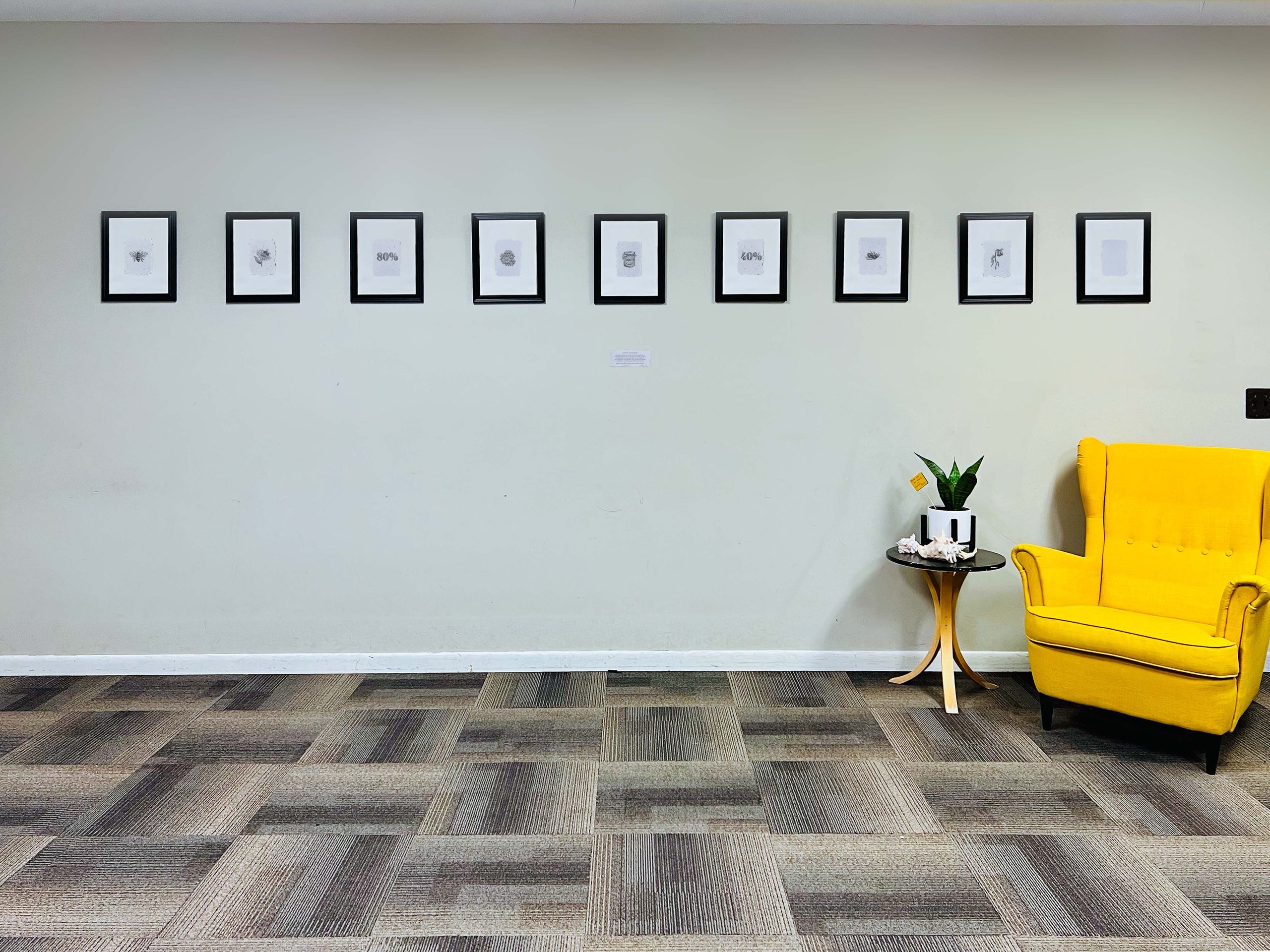 08 Modern office interior with yellow chair, small side table with plant, and row of nine framed artworks on white wall