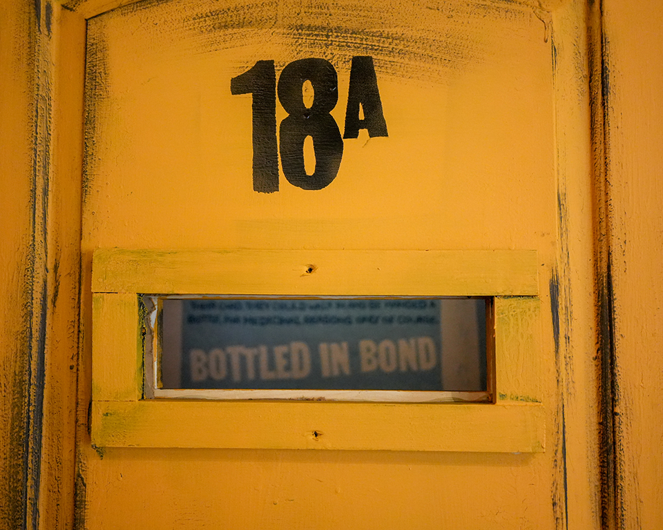 Yellow painted door with 18A number and BOTTLED IN BOND text visible through window panel