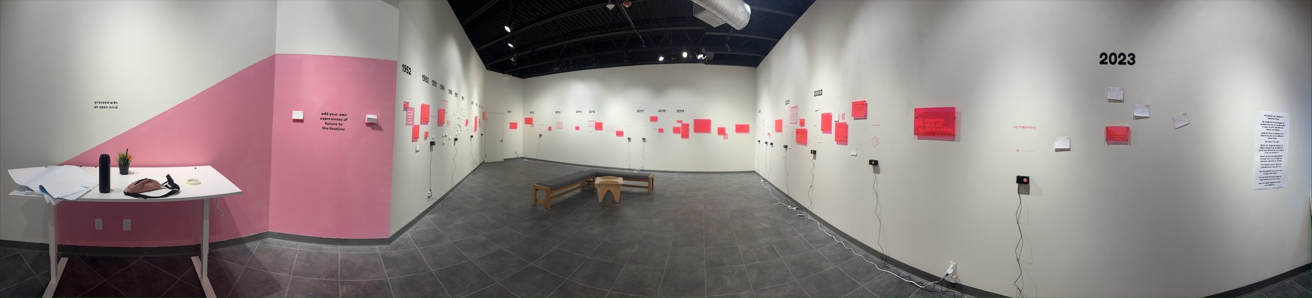 Modern art gallery exhibition with pink wall elements, red artwork displays, and wooden bench in center space