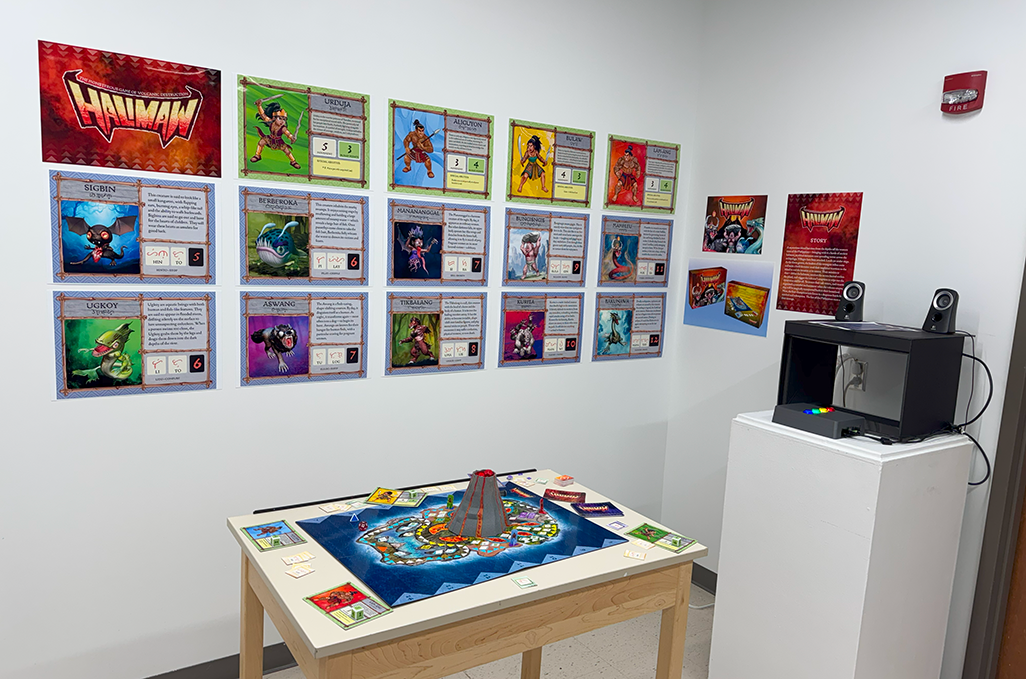 Gaming display featuring Gunman cards on wall, board game on wooden table, and retro gaming setup on white pedestal.
